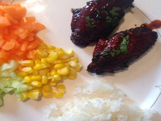Assiette avec deux morceaux de viande glacés, riz blanc et brunoise de légumes colorés