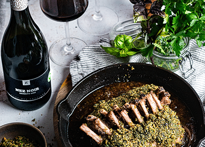 Carré d'agneau en croûte d'herbes dans une poêle en fonte, accompagné d'une bouteille de Nez Noir Rouvinez