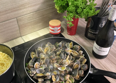 Poêle de palourdes ouvertes avec bouteille de vin rouge et persil frais sur plan de travail