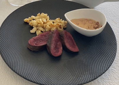 Tranches de viande rouge servies avec spätzle et sauce dans un bol blanc sur assiette noire