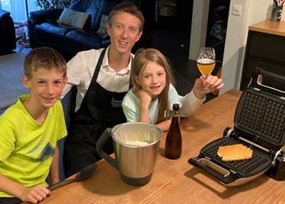 Vigneron en tablier posant avec deux enfants autour d'un gaufrier et d'une bouteille à la maison